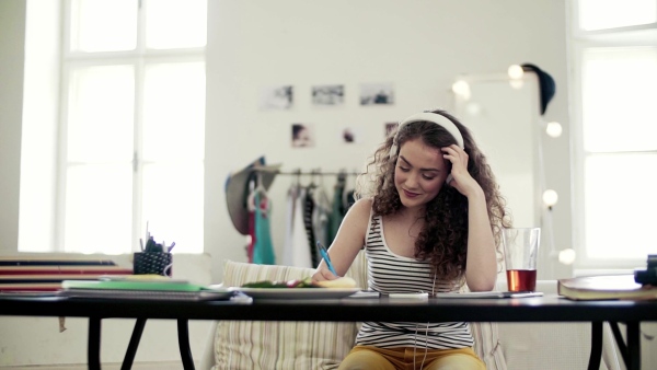 A young teenage girl with headphones sitting indoors, listening to music. Slow motion.