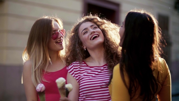 Young teenage female friends with ice cream standing outdoors in town, laughing. Slow motion.