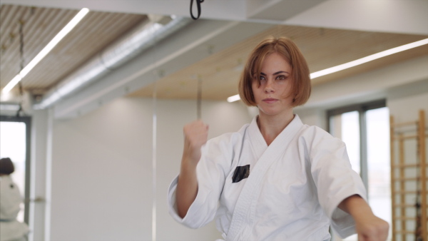 Front view of young woman practising karate indoors in gym.