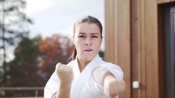 An attractive young woman practising karate outdoors on terrace.