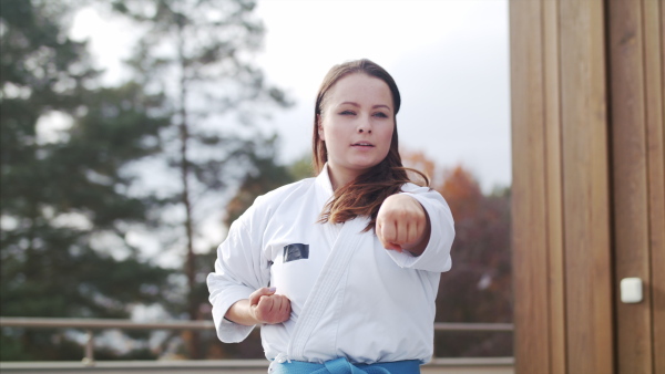 An attractive young woman practising karate outdoors on terrace.