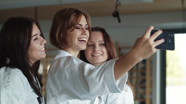 Group of young karate women with smartphone indoors in gym, taking selfie.