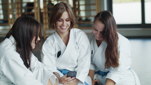 A group of young karate women with smartphone indoors in gym, resting.