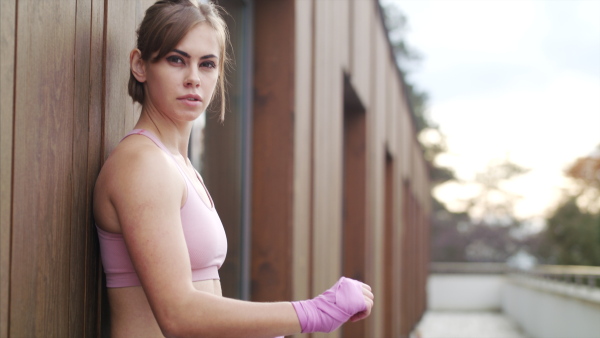 A young sportswoman standing outdoors on terrace, resting, looking at camera.