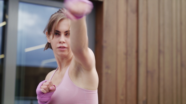 Concentrated young woman doing exercise outdoors on terrace, boxing.