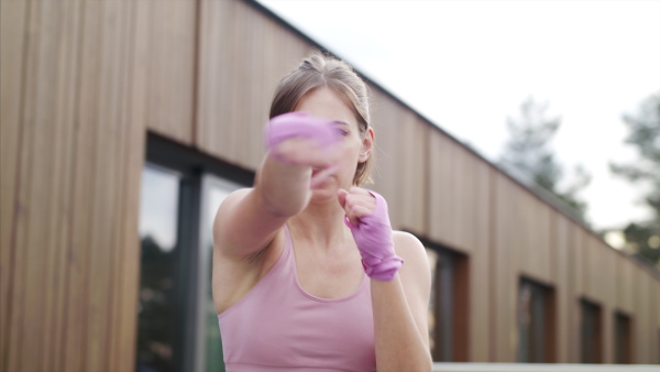 Concentrated young woman doing exercise outdoors on terrace, boxing.