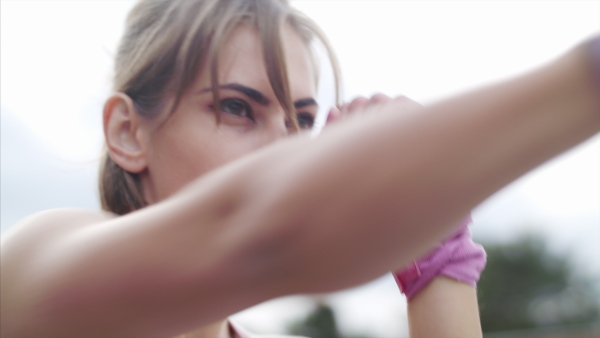 Concentrated young woman doing exercise outdoors on terrace, boxing.