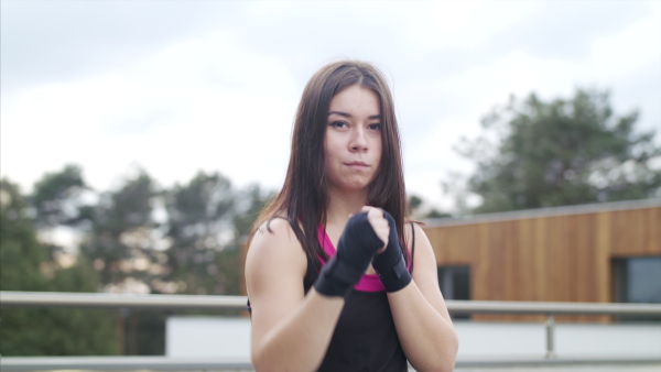 Concentrated young woman doing exercise outdoors on terrace, boxing.