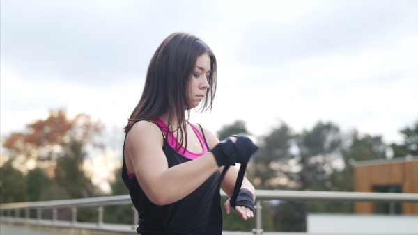 Young woman wrapping hands outdoors on terrace before boxing exercise.