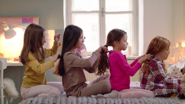 Group of happy small girl friends on kids sleepover slumber party, plaiting hair.