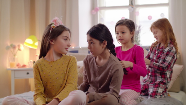 Group of small girls friends in pajamas playing on bed on slumber party.