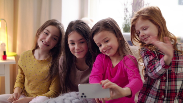 Group of small girls friends with smartphone on bed on slumber party, taking selfie. Slow motion.