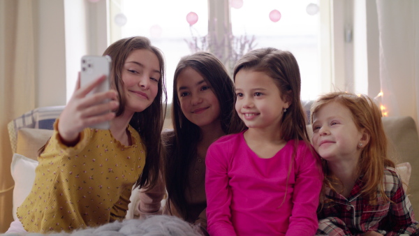 Group of small girls friends with smartphone on bed on slumber party, taking selfie. Slow motion.