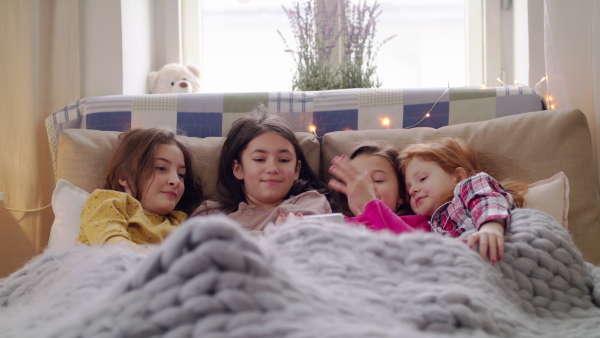 Group of small girls friends with smartphone on bed on slumber party, watching videos. Slow motion.