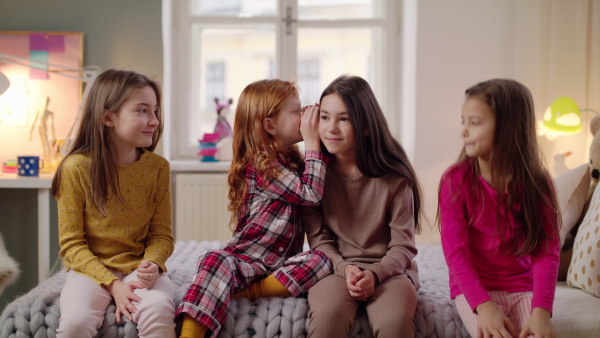 Group of small girls friends in pajamas playing on bed on slumber party.