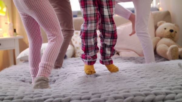 Midsection of group of small unrecognizable girls friends jumping on bed on slumber party.