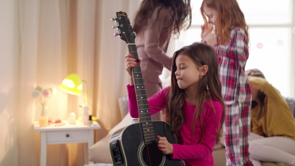 Group of small girls friends playing guitar and jumping on bed on slumber party.