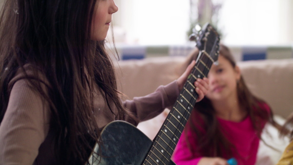 Group of small girls friends playing guitar and singing on bed on slumber party.