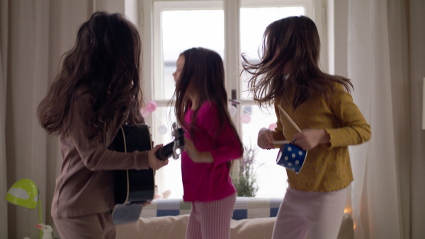 Group of small girls friends playing guitar and jumping on bed on slumber party.