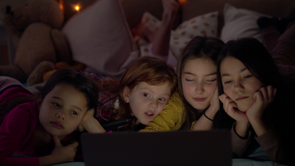 Front view of group of small girls friends with laptop on bed on slumber party, watching.