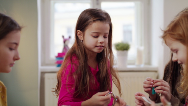 Group of small girls friends in pajamas playing on bed on slumber party, trying earrings.