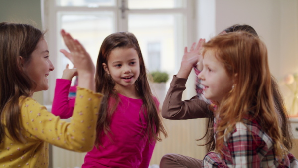 Group of happy small girls friends playing on bed on slumber party, giving high five.