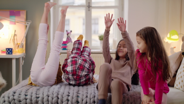 Group of small girls friends in pajamas playing on bed on slumber party, having fun.