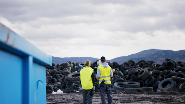 Rear view of man and woman workers on landfill, waste management and environmental concept.