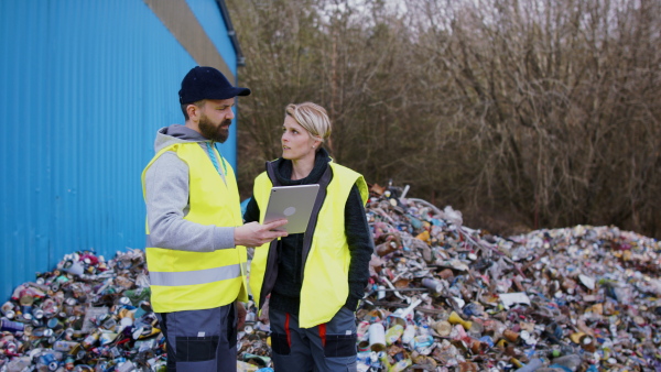 Man and woman workers with tablet on landfill, waste management and environmental concept.