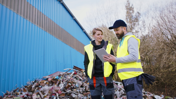 Man and woman workers with tablet on landfill, waste management and environmental concept.