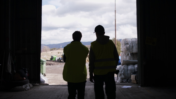 Rear view of man and woman workers walking on landfill, waste management and environmental concept.