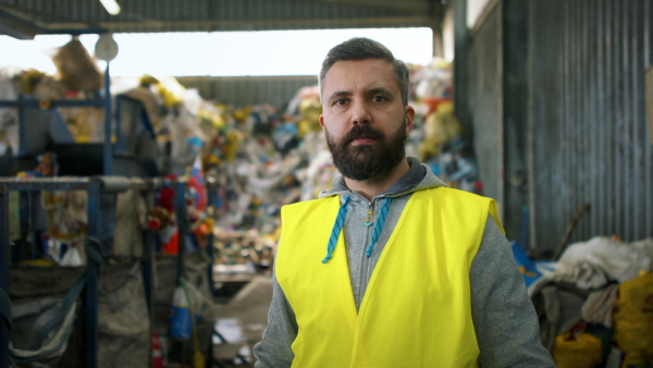 Front view of mature worker standing on landfill, waste management concept.