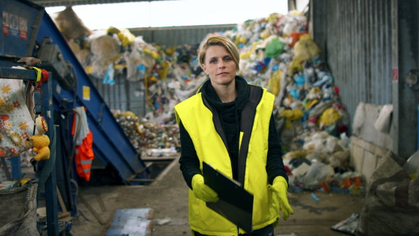 Front view of woman worker walking on landfill, waste management concept.