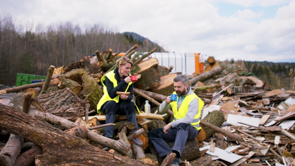 Man and woman workers having snack break on landfill, waste management concept.