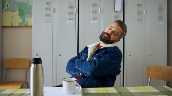 Portrait of tired man worker sitting by lockers, sleeping on chair.