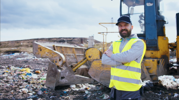 Front view of worker looking at camera on landfill, waste management and environmental concept.