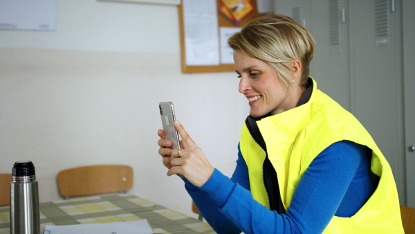 Side view of woman worker sitting by lockers, using smartphone at break.