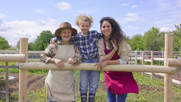 A grandmother with her daughter and granddaughter standing on field and looking at camera. Community farming concept.