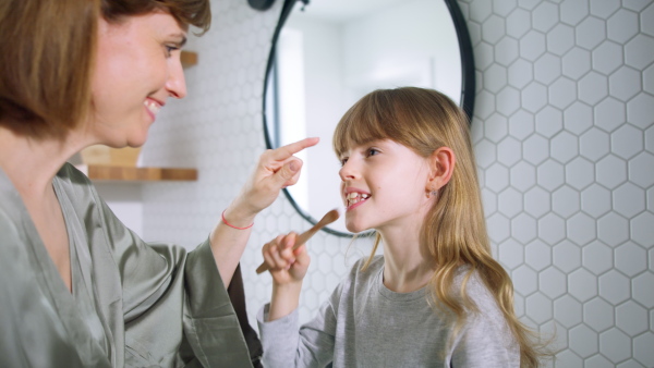 Little daughter tooth brushing and mother hugging her in the morning.