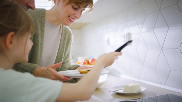 A mother with daughter at home making a pancakes together.