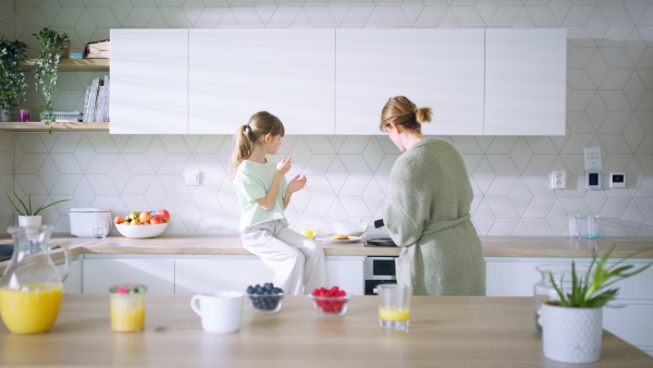 A mother with daughter at home making a pancakes together.