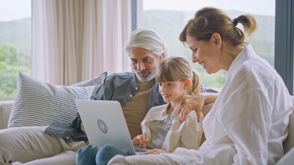 A beautiful family at home, sitting on sofa and watching movie on laptop together.