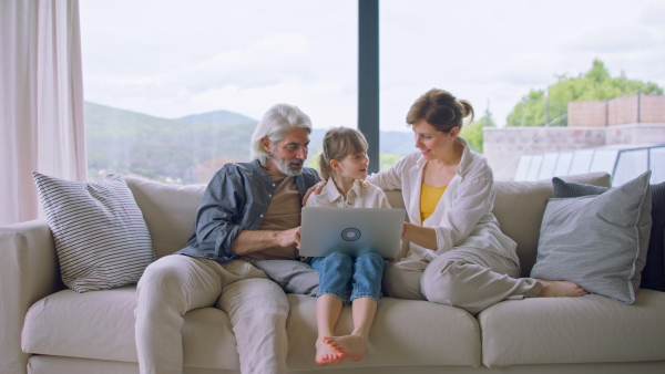 A beautiful family at home, sitting on sofa and watching movie on laptop together.