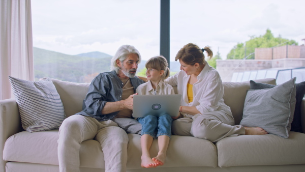 A beautiful family at home, sitting on sofa and watching movie on laptop together, looking at camera.