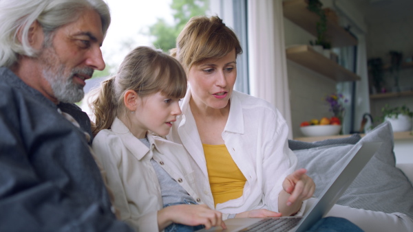 A beautiful family at home, sitting on sofa and watching movie on laptop together.