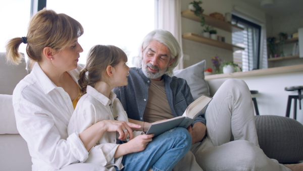 A beautiful family at home, sitting on sofa and reading a book together.