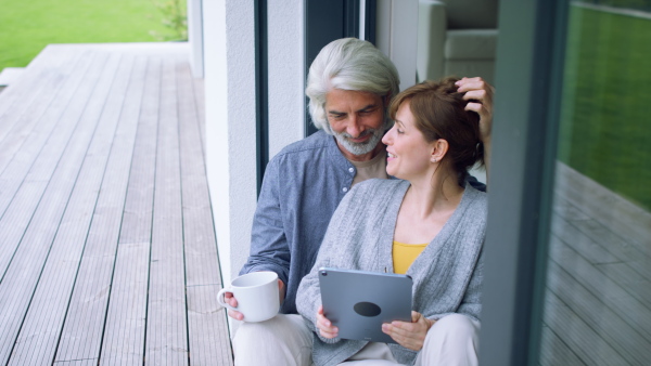 A beautiful couple at home, sitting on terrace and watching movie on tablet together.