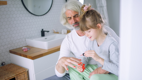 A playful daughter nailpolisihing fathers nails in the bathroom.