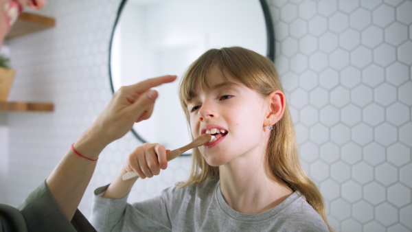 Little daughter tooth brushing and mother hugging her in the morning.