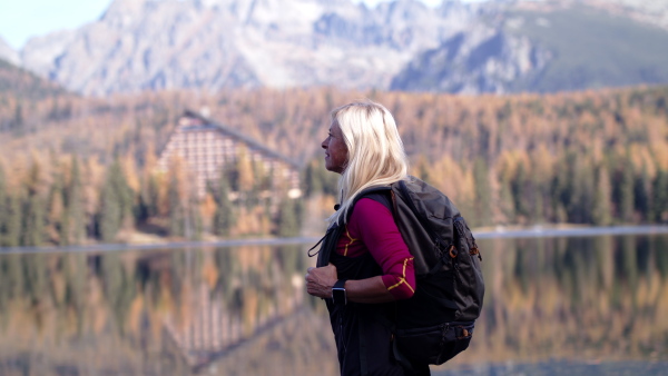 Attractive active senior woman with backpack standing outdoors in nature, hiking. Slow motion.